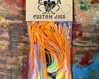 Könnte beinhalten: Eine Packung mit orangefarbenen, gelben und blauen, maßgefertigten Angeljig-Röcken. Die Packung ist mit "English Angling" und "Custom Jigs" beschriftet.