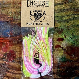 Puede incluir: Un paquete de faldas de jigging personalizadas de color rosa, blanco y amarillo con el texto "ENGLISH ANGLING E.A.A. CUSTOM JIGS" en la parte delantera.
