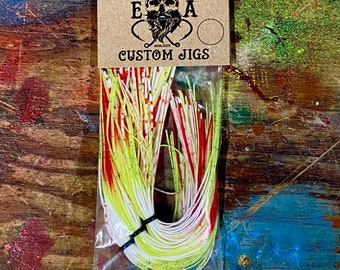 Könnte beinhalten: Eine Packung mit maßgefertigten Angelködern von English Angling. Die Köder sind weiß, rot und gelb mit einem grünen Glitzerfinish. Die Packung ist mit "English Angling" und "Custom Jigs" beschriftet.