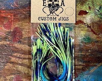 Könnte beinhalten: Eine Packung mit blauen, grünen und gelben, maßgefertigten Angelködern. Die Verpackung ist mit "English Angling" und "Custom Jigs" beschriftet.