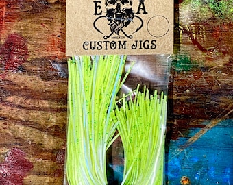 Könnte beinhalten: Eine Packung grünes und weißes Angeljig-Material mit dem Text "ENGLISH ANGLING E A CUSTOM JIGS" auf dem Etikett.