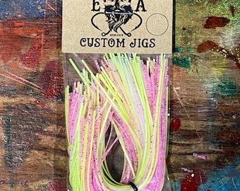 Könnte beinhalten: Eine Tüte mit pinkfarbenen und gelben, maßgefertigten Jigging-Strängen zum Angeln. Die Tüte trägt ein Etikett mit der Aufschrift "English Angling" und "Custom Jigs".