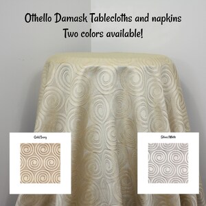May include: A round tablecloth with a swirling pattern in gold and ivory. The tablecloth is made of damask fabric and is available in two colors: gold/ivory and silver/white. Othello Damask Tablecloths and napkins. Two colors available!