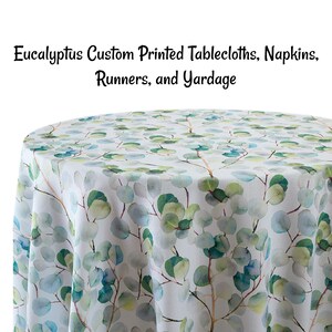 May include: A white tablecloth with a watercolor print of eucalyptus leaves in shades of green, blue, and yellow. The tablecloth is round and has a smooth, linen-like texture.