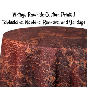 May include: A close-up of a brown and orange textured fabric tablecloth. The fabric has a distressed, vintage look.  Vintage Rawhide Custom Printed Tablecloths, Napkins, Runners, and Yardage.