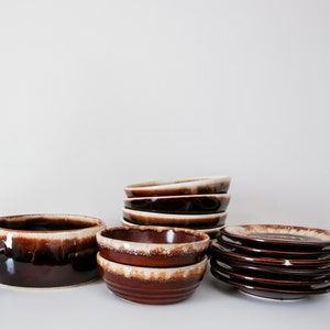Peut inclure: Un ensemble de bols et d'assiettes en céramique émaillée brun et blanc. Les bols sont empilés et les assiettes sont empilées. Les bols et les assiettes ont un glaçage brun avec un bord blanc.