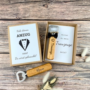 Könnte beinhalten: Ein Holz-Flaschenöffner mit der Aufschrift "Trauzeuge" eingraviert. Der Flaschenöffner befindet sich in einer Schachtel mit einer Karte, auf der "Willst du mein Trauzeuge sein?" steht. Die Karte zeigt auch ein Smoking-Motiv mit dem Text "Hole deinen Anzug raus! Du wirst gebraucht!"