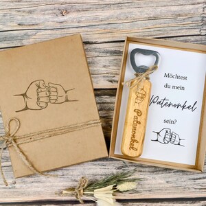 May include: A wooden bottle opener with the word "Patenonkel" engraved on it, presented in a kraft paper box. The box and the card inside feature a fist bump graphic. The text on the card reads "M&ouml;chtest du mein Patenonkel sein?"
