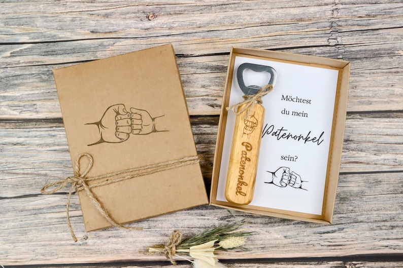 May include: A wooden bottle opener with the word "Patenonkel" engraved on it, presented in a kraft paper box. The box and the card inside feature a fist bump graphic. The text on the card reads "M&ouml;chtest du mein Patenonkel sein?"