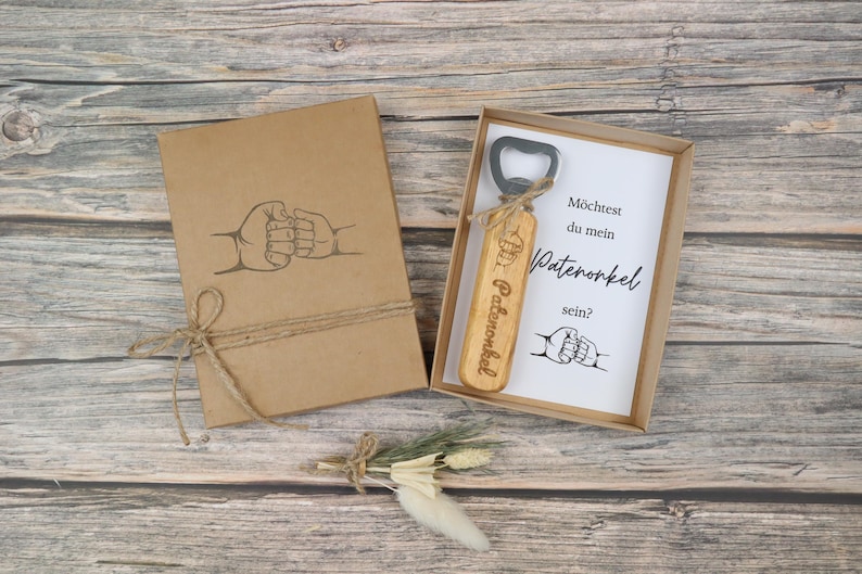 Braune Geschenkbox mit modernem Motiv auf der Vorderseite und graviertem Flaschenöffner aus Holz und Edelstahl – Geschenkset zur Patenonkel-Frage.