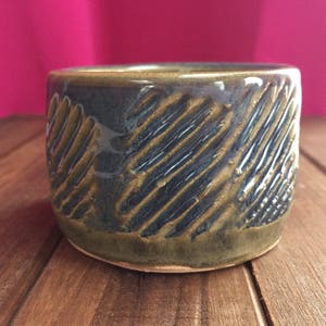 May include: A small, ceramic bowl with a dark blue glaze and a brown, textured pattern. The bowl is sitting on a wooden surface.