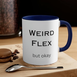 Puede incluir: Taza de café blanca con borde y asa azules. La taza tiene texto negro que dice "WEIRD FLEX but okay".