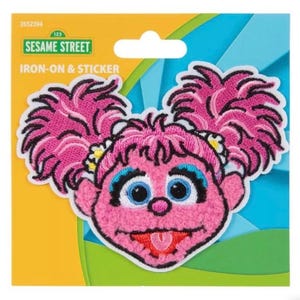 May include: An iron-on and sticker featuring the Sesame Street character, Abby Cadabby. The patch has a pink face, hair, and tongue, with blue eyelashes and eyes. The patch is on a colorful background with the Sesame Street logo.