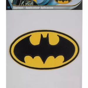 May include: A yellow and black iron-on patch featuring the Batman logo. The logo is a stylized bat silhouette inside an oval. The patch is packaged on a white card with the text "Applique - Application - Aplicacion" and "C&D Visionary Inc."