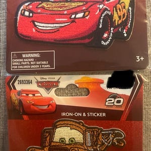May include: Two Disney Pixar Cars iron-on and sticker patches in original packaging. The top patch features the red race car Lightning McQueen with the number 95. The bottom patch depicts the brown tow truck Mater with green eyes and a wide smile.