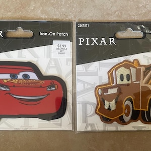 May include: Two iron-on patches featuring characters from the Disney Pixar movie Cars. The first patch is red and features Lightning McQueen, a race car with the number 55 on the side. The second patch is brown and features Mater, a tow truck with a large smile. Both patches have the words "PIXAR" and "Iron-On Patch" printed on them.