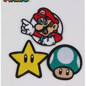 May include: Three iron-on patches featuring Super Mario characters. The patches are a yellow star with a face, a green mushroom with a white top and a face, and Mario with his signature red hat and overalls.
