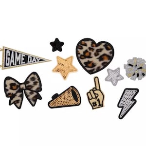 May include: A collection of ten embroidered patches featuring a pennant with the text GAME DAY, a leopard print heart and bow, a gold sequined star, a black star, a megaphone, a foam finger with the number 1, a silver star, a pom-pom, and a lightning bolt.