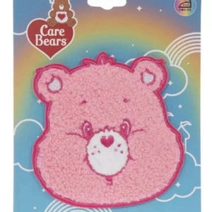 May include: A pink Care Bears iron-on/sticker patch featuring a smiling bear face with a white heart on its belly. The patch is on a blue background with a rainbow and Care Bears logo.