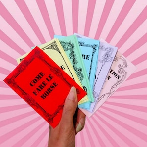 May include: A hand holds a fan of colorful cards against a pink background with white stripes. The cards are red, yellow, green, blue, and lavender, each with black text and decorative borders. The red card reads "COME FARE LE BORSE."