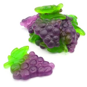May include: Gummy candy shaped like grapes, with green leaves and purple and green fruit. The candy is arranged in clusters and individual pieces, with a white background.