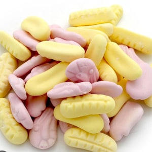 May include: A collection of sweets in shades of yellow and pink. The candies are in various shapes, including bananas and corn cobs. The image is a close-up shot against a white background, showcasing the colorful assortment of treats.