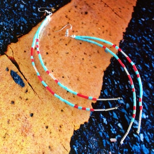 May include: A pair of long, dangling earrings with turquoise and red beads. The earrings are made with silver wire and have a simple hook closure.