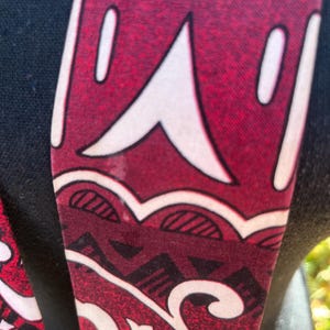 May include: Close-up of a patterned fabric with a burgundy background and white and black geometric designs. The fabric is draped over a black surface, showcasing the intricate patterns and textures.