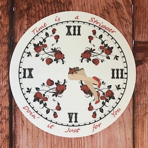 May include: A white clock face with black Roman numerals and a black border. The clock face has a red floral design and a red inscription that reads "Time is a Stripper Doin' it Just for You".