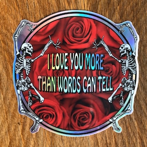 May include: A holographic sticker with two skeletons dancing around a circle of red roses. The text reads "I love you more than words can tell."