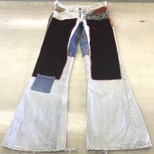 May include: Light blue denim bell bottom pants with patchwork details. The patches include a dark brown velvet fabric, a floral patterned fabric, and a blue denim fabric.