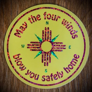May include: A yellow round sticker with a red, green, and white compass rose design in the center. The text around the compass rose reads "May the four winds blow you safely home".