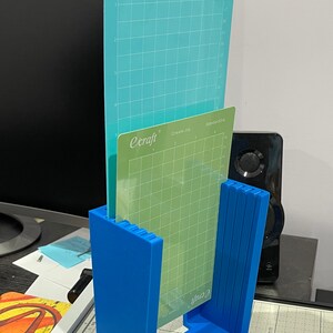 May include: A blue plastic stand holds two cutting mats. The top mat is light blue with the text "ecraft Create Joy LightGrip". The bottom mat is green with the text "ecraft Create Joy StandardGrip".