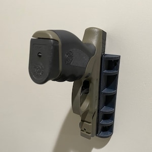 May include: A black and green handgun mounted on a wall with a black magnetic holder.