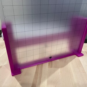 Op de afbeelding: Een paarse snijmat met een rasterpatroon. De mat wordt op een set paarse steunen geplaatst.
