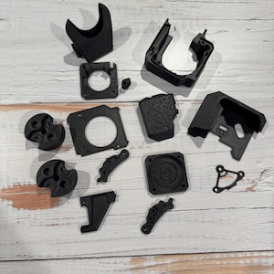 May include: A set of 12 black 3D printed parts for a 3D printer. The parts include a fan shroud, a fan mount, a motor mount, a nozzle holder, a heat sink, and other small parts.