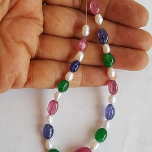 May include: A strand of oval-shaped beads in white, green, pink, and blue. The beads are strung on a silver wire.
