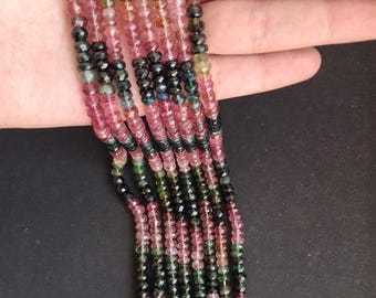 May include: Strands of gemstone beads in shades of pink, green, and black. The beads are small and faceted, creating a sparkling effect. The gemstones are strung together, forming multiple strands. The background is a dark, solid color.