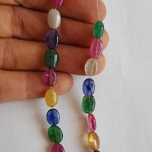 May include: A strand of oval-shaped gemstone beads in various colors, including green, pink, blue, and yellow. The beads are strung on a thin wire.