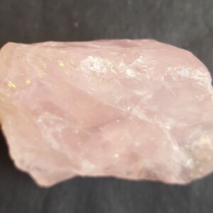 Peut inclure: Un gros cristal de quartz rose brut avec une apparence translucide et vitreuse. Le cristal a une surface naturelle non polie avec des inclusions visibles.