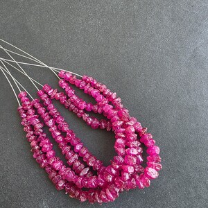 May include: Several strands of raw, pink ruby gemstone beads. The beads are irregularly shaped and strung on thin, silver-coloured wire. The gemstones have a rough, natural texture and a deep, saturated colour, ideal for jewellery making.