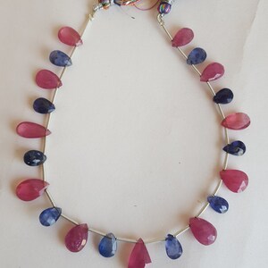 May include: A strand of gemstone beads, featuring alternating pink and blue pear-shaped beads. The beads are strung on a silver wire.