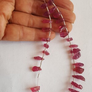 May include: A strand of pink ruby gemstone beads strung on a silver wire. The beads are irregular in shape and have a rough, natural finish.
