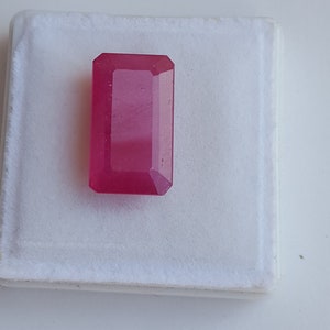 May include: A vibrant pink gemstone with a rectangular emerald cut. The gemstone is displayed on a white background.