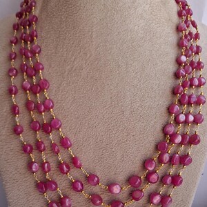 Puede incluir: Un collar de múltiples hilos hecho de cuentas de piedras preciosas rosadas y eslabones de cadena de oro. El collar está en capas y presenta una variedad de tamaños de cuentas.