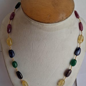 Puede incluir: Un collar de cadena de oro con piedras preciosas ovaladas alternas en tonos de verde, azul, morado y amarillo.