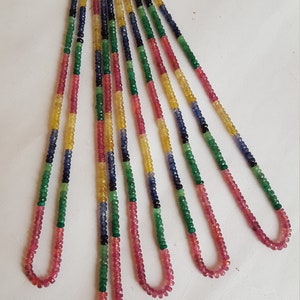 Può includere: Un set di sei fili di perline di pietre preziose colorate. Le perline sono disposte a ventaglio e sono fatte di pietre preziose rosa, verdi, blu e gialle.