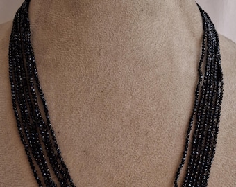 May include: A multi-strand necklace made of black faceted beads. The necklace is displayed on a mannequin.