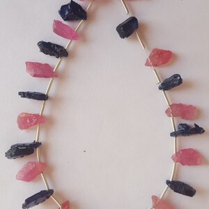 May include: A strand of gemstone beads, featuring alternating pink and blue rough cut stones. The beads are strung on a silver wire.