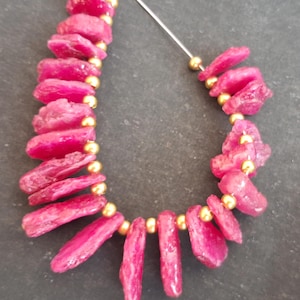 May include: A strand of pink ruby gemstone beads with gold spacers. The beads are irregular in shape and have a rough, natural texture.